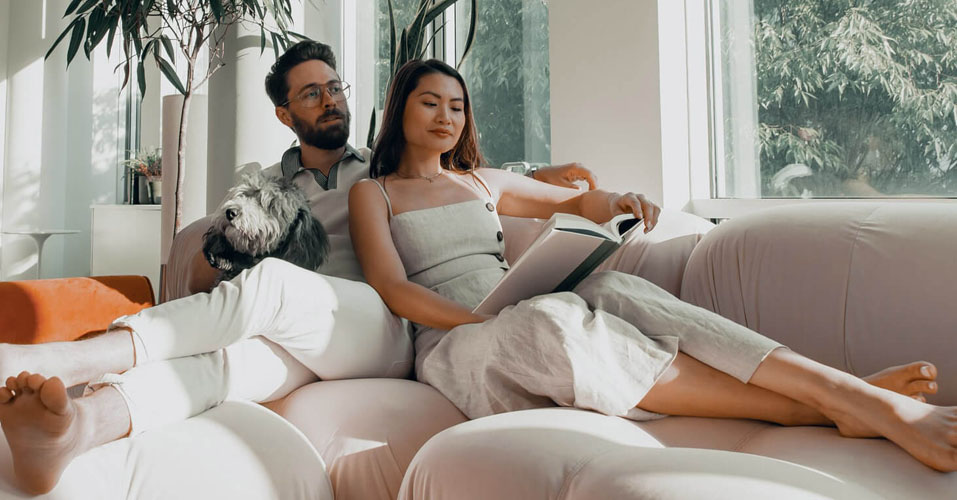 A couple relaxing on couch reading book with dog on lap